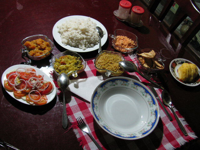 Rice served along with three vegetable curries, coconut sambol, salad, papadam and pineapple. Photo Source